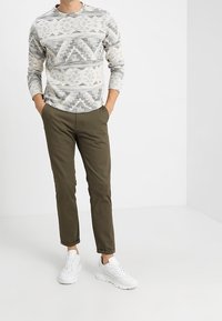 Felpa a maniche lunghe con texture e motivo geometrico grigio e bianco, abbinata a pantaloni aderenti verde oliva e sneakers bianche.