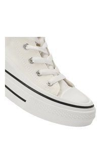 Zapatilla alta de lona blanca con puntera redonda, cordones planos, ojales plateados y suela de goma negra como acento. Superficie texturizada y acabado suave.