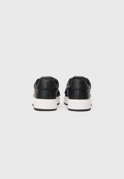 Zapatillas de cuero negro con suela blanca, con una textura suave, detalles de costura y un tirador en el talón. Vista desde atrás.