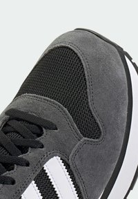 Γκρι αθλητικό παπούτσι με συνδυασμό σουέτ και διχτυωτού υλικού, μαύρα κορδόνια, λευκές ρίγες και υφασμέν�ο λαστιχένιο πάτο με στρογγυλεμένο σχήμα.