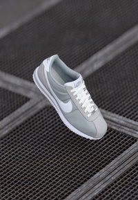 Gray Nike sneaker featuring a smooth upper, white accents, textured overlays, and a rubber sole with zigzag pattern. Laces are white.
