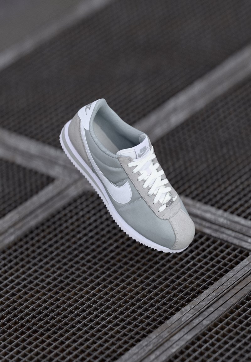 Gray Nike sneaker featuring a smooth upper, white accents, textured overlays, and a rubber sole with zigzag pattern. Laces are white.