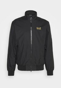 Svart bomberjacka med dragkedja, ståkrage, elastiska ärmslut och sidofickor. Har en guld EA7-logotyp på bröstet. Slät material.