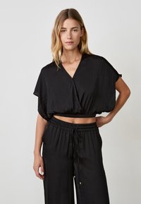 Top corto nero con scollatura a V, maniche ampie e vita arricciata. Abbinato a pantaloni a gamba larga dello stesso colore con vita elastica e cordino.