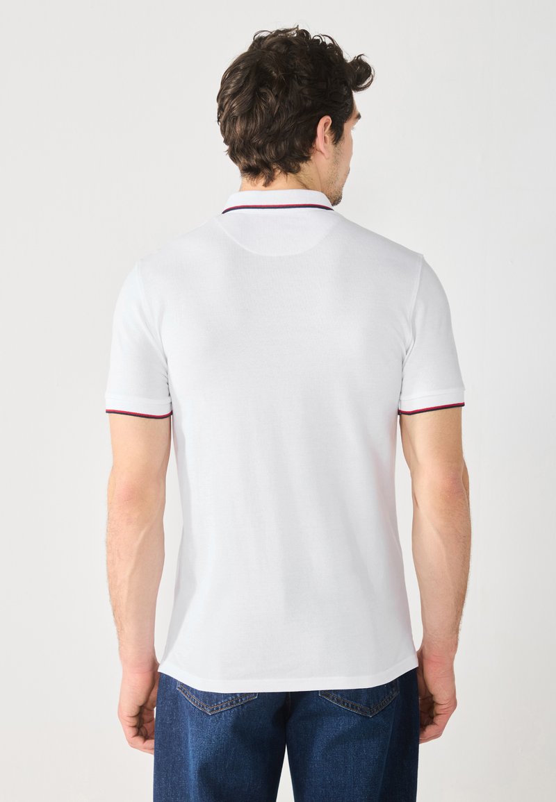 Weißes Poloshirt mit kurzen Ärmeln, das eine kontrastierende rot und navyblaue Streifen an Kragen und Ärmelsäumen aufweist. Weicher Stoff.