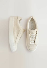 Baskets en tricot beiges avec une tige texturée, semelles en caoutchouc blanches et lacets plats. Elles présentent un bout rond et des détails de couture subtils.