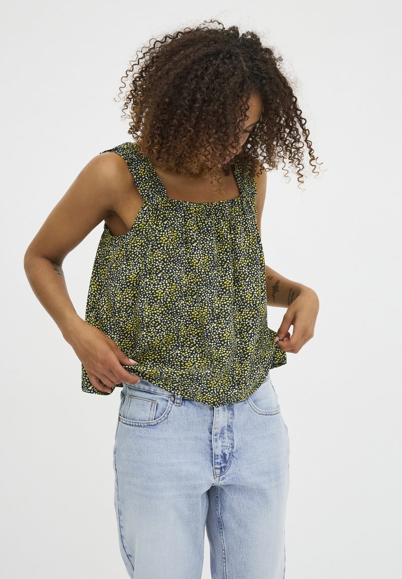 Ärmvärmare med blommönster och fyrkantig halsringning, tillverkad av lätt tyg i svarta, gula och gröna nyanser. Avslappnad passform.