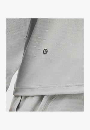 Light gray athletic top featuring textured fabric, a round neckline, and a small logo on the left side. Visible seams and layered design.