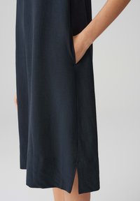 Dark blue linen dress with side pockets, knee-length, featuring a slit at the hem for ease of movement. Smooth texture and minimalist design.