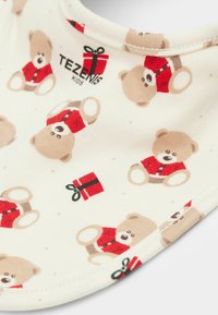 Bavetta di cotone con sfondo crema e motivo ripetuto di orsacchiotti beige con abiti rossi e piccoli pacchetti regalo.