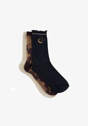 Mixed-color socks: one dark navy with a golden moon emblem, one beige with a maroon floral pattern. Finished with a ruffled cuff.