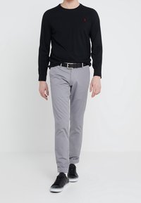 Svart långärmad skjorta med en liten röd logotyp, grå byxor och svarta sneakers. Enkel design, kroppsnära passform, slät textur.