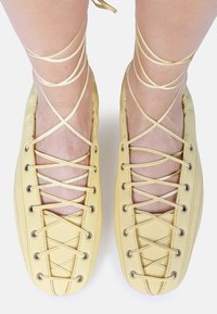 Chaussures jaunes à lacets avec une finition en cuir souple, dotées de sangles croisées et d'œillets en métal pour un maintien sécurisé. Accentuées par des lacets fins.