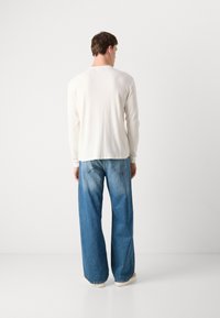 Witte lange mouwen geribbelde shirt gecombineerd met losse blauwe jeans. Het shirt heeft een ronde hals, en de jeans hebben een vervaagde was en ruime pijpen.