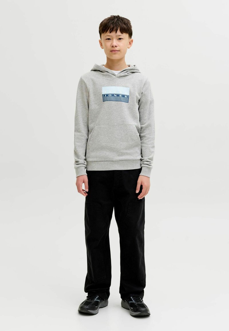 Boy standing facing forward wearing a grey hoodie with "JONES" logo, black pants, and black sneakers on a plain light background.