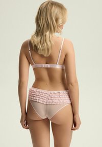Jasnoróżowy zestaw bielizny składający się z gładkiego, satynowego biustonosza z regulowanymi ramiączkami oraz dopasowanych majtek z warstwowym detalem falbanek.