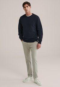 Sweatshirt cu guler rotund de culoare bleumarin, fabricat dintr-un material texturat, asociat cu pantaloni slabi de culoare bej deschis și adidași de culoare verde mentă. Design simplu cu manșete cusute.