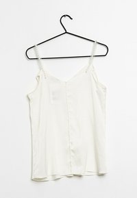 Witte satijnen camisole met dunne bandjes versierd met parelaccenten, met een V-hals en een vloeiende pasvorm, hangend aan een zwarte haak.