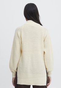 Pull tricoté couleur crème avec une coupe décontractée, manches longues et un motif texturé. Comprend un col et un ourlet côtelés.