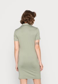 Vestido curto justo em tecido verde claro. Apresenta gola tipo polo e mangas curtas. Textura suave com detalhes mínimos.