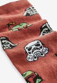 Stickade strumpor i rostfärgad nyans med flerfärgad pixeldesign av en stormtrooper, Darth Vader och Boba Fett på en texturerad bakgrund.