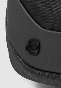 Bolsa de tela negra con textura y borde liso y redondeado, con un logotipo minimalista en gris oscuro. Detalles incluyen costuras en contraste.