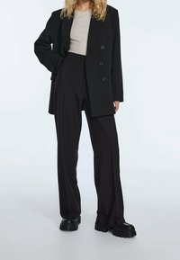 Black double-breasted blazer with notched lapels paired with high-waisted black trousers, showcasing a relaxed fit. Chunky black footwear.