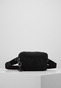 Zwarte stoffen heuptas met een ritsluiting, verstelbare riem, rubberen logodetail en een kleine charmaccent. Gladde textuur met een compact ontwerp.
