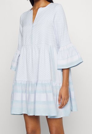 Femme portant une robe ample à motif bleu clair et blanc avec des manches cloche trois-quarts et un col en V.