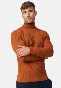 Pull à col roulé en orange brûlé, avec un motif zigzag texturé, des poignets et un ourlet côtelés. Fabriqué en tissu doux et extensible.