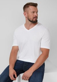 Witte t-shirt met korte mouwen en een V-hals ontwerp, gemaakt van een soepele stof. Het shirt heeft subtiele branding op de borst.