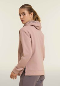 Felpa rosa chiaro realizzata in tessuto morbido, con un rivestimento grigio a motivo nella cappuccio, spacchi laterali all'orlo e una vestibilità comoda.