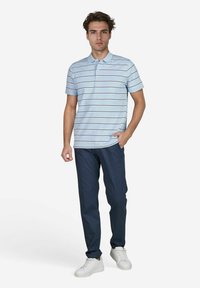 Polo shirt à rayures bleu clair avec des manches courtes, associé à un pantalon bleu foncé et des baskets blanches. Le design présente un col classique.