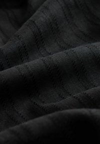 Schwarzer Stoff mit dezenten horizontalen Texturstreifen und weichen Falten, die ein wellenförmiges Muster erzeugen.