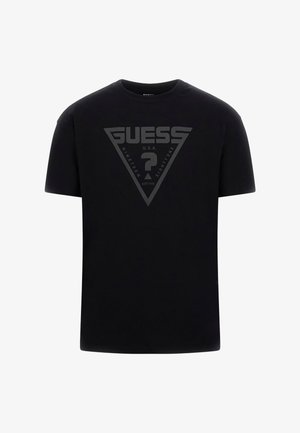 Fekete pamut póló, amelyen egy nagy háromszög alakú logó látható a "GUESS" és a "NINETEEN EIGHTY-ONE" felirattal, matt felülettel, középen elhelyezve.