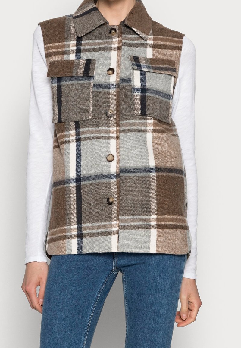 Brun och grå rutigt väst av flanell, med två bröstfickor, krage och framknäppning med knappar. Bärs över en vit långärmad skjorta.