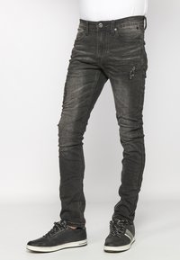Dark gray denim jeans with a slim fit, featuring distressed accents, five pockets, and a button closure. Paired with black sneakers.