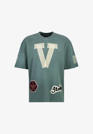 Green cotton oversized t-shirt featuring a large cream "V" with tape accents, and three embroidered patches: star, hexagon, and "Italy."