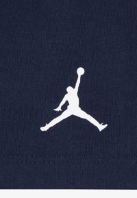 Tmavě modrá látka s bílou siluetou skákající postavy držící basketbalový míč, výrazně umístěná na spodní části.