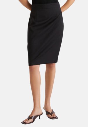 Gonna a tubino nera al ginocchio indossata da una persona con gambe nude, abbinata a sandali con tacco a infradito marrone scuro.