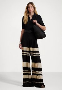 Svart ribbad topp med korta ärmar, vida plisserade byxor med svarta och cremefärgade ränder, svart flätad handväska, silverarmbandsmanschett och bältespänne.