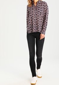 Langärmlige gemusterte Bluse in Marineblau mit pinken Blumenmustern, kombiniert mit schwarzen Skinny-Jeans und weißen Sneakers. Die Bluse hat einen Kragen und eine Knopfleiste.