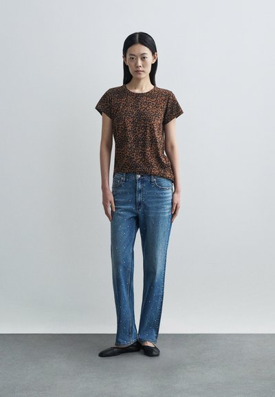 Καφέ μπλουζάκι με λεοπάρ σχέδιο και κοντά μανίκια, συνδυασμένο με μπλε τζιν με διάσπαρτες διακοσμήσεις και ίσια γραμμή στα πόδια. Μαύρα φλατ παπούτσια.