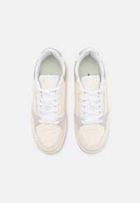 Sneaker bianchi e beige con tomaia in pelle liscia, punta forata e accenti grigio chiaro. Presentano lacci bianchi piatti e colletto imbottito.