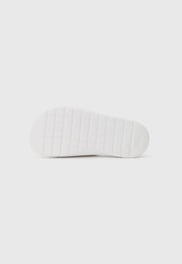 Semelle en caoutchouc blanc avec un motif de grip texturé, comportant un logo près du talon et un bout arrondi. Surface lisse avec un design minimaliste.