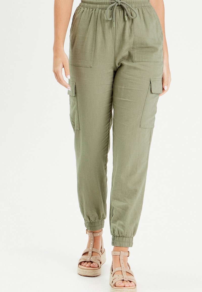Pantalon cargo vert olive avec une taille élastique, un cordon de serrage et des poches latérales ; associé à des sandales à brides beige clair.