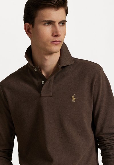 Smeđi dugosleeve polo majica od teksturirane tkanine, s dvobrojnim kopčanjem, otvorenim ovratnikom i malim zlatno vezivanim logotipom na prsima.