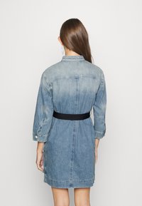 Denim skjortklänning med långa ärmar, ljusblå färg, ett svart bälte i midjan och rak skärning. Har knappade manschetter och krage.