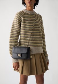 Black leather handbag with a structured design, gold hardware, chain strap, and a front flap closure featuring a logo. Striped sweater and pleated skirt.