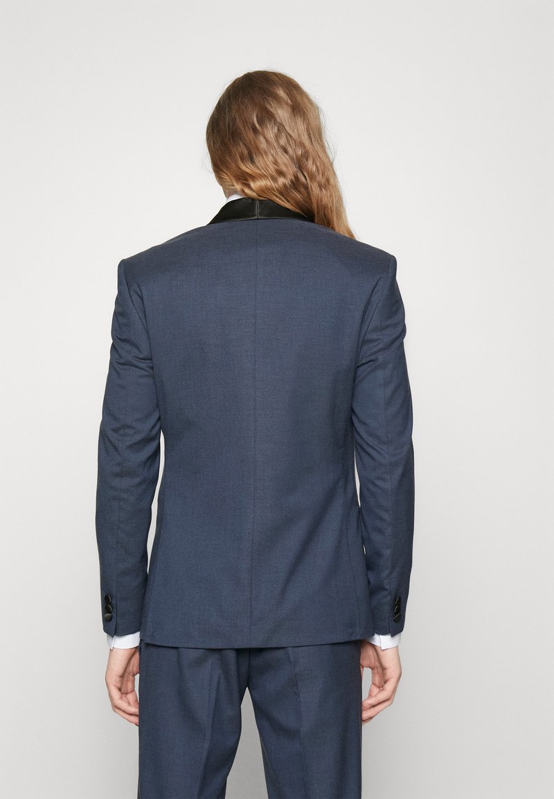 Giacca da abito blu navy con vestibilità slim, caratterizzata da un colletto in satin nero, tessuto testurizzato e polsini abbottonati. Vista dal retro, che mostra linee pulite.